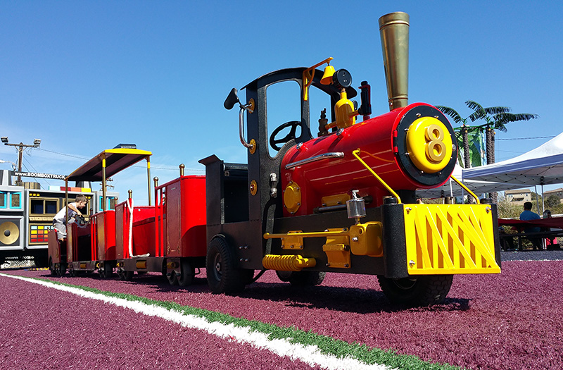 Bright red miniature steam locomotive with yellow front grating and black cab on purple ground under a clear blue sky, number 8 visible on the front headlamp plate.